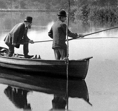 Black and white photograph of two adults fishing over the side of a rowing boat