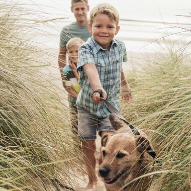 Photograph of two children, and an adult, on a dog walk through sand dunes