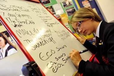 Photograph of teenager writing things, such as 'Eco savers', on a whiteboard 