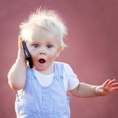 Photograph of toddler holding a mobile phone to their ear