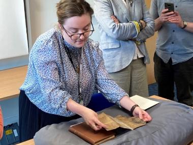 Photo of Georgina Rowley unfolding an old, fragile, piece of paper which is resting on a large cushion