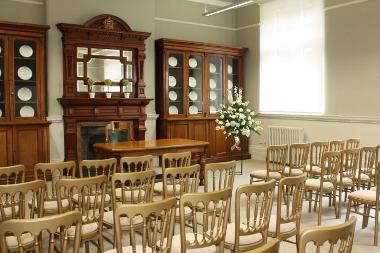 Photo of the Supper Room at Great Yarmouth Town Hall including gold chairs in rows, wooden furniture with mirror and plates