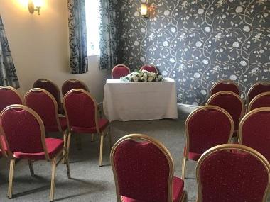 Photo of Franklin Room Thetford showing floral wallpaper, red chairs in rows, and a small white cloth-covered table