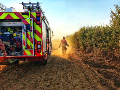Fire engine and fire fighter spraying a crop fire with water