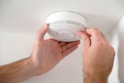 Photograph of hands fixing a smoke alarm onto a ceiling. 