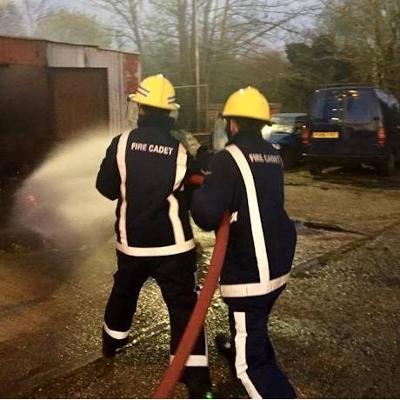 Two fire cadets in uniform and helmets using a fire hose