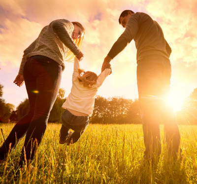 Two parents holding child's hands in a grassy field 