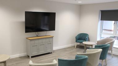 Wall mounted television with armchairs and tables in a communal area of Swallowtail Place 