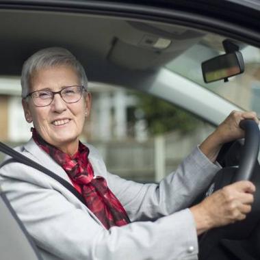 Photograph of older driver smiling, sitting behind the wheel of a car