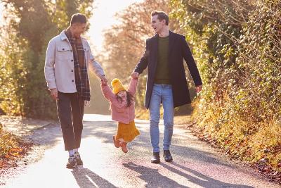Photograph of two adults walking along playfully swinging a smiling child between them