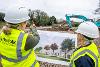 Two workers look at an illustration while a digger works on the development in the background