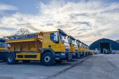Six yellow grit spreading trucks lined up outside a depo