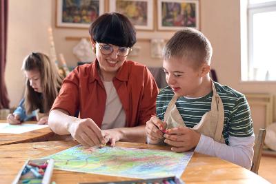 Support worker sitting at desk with young boy doing artwork
