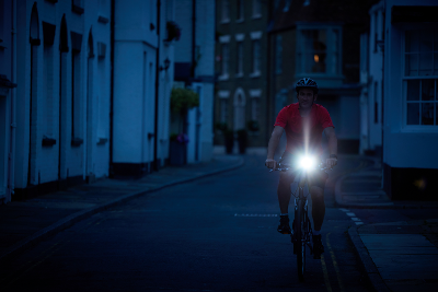 Photograph of someone riding a bicycle with a front light in the semi-darkness