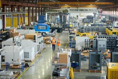 Man wearing hardhat walking across production workshop accompanied by female factory employee