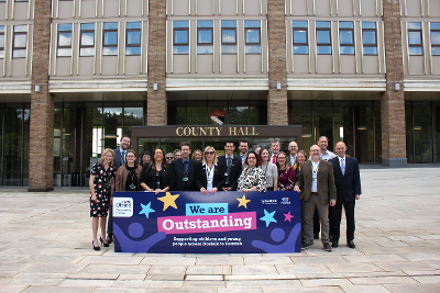 Council staff stand behind a banner that reads 'We are Outstanding'