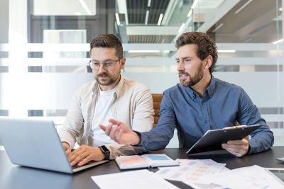 Two men sitting at a desk looking at a computer screen